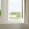 A close-up view of a white window frame with a partially open window, showing a blurred outdoor scene. Podgląd zdjęcia produktu