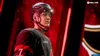 A hockey player in uniform, looking to the side, with red lighting in the background. Produktbild-Vorschau