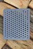 A square cast iron grate with many holes is placed on top of stacked firewood. Voir les images du produit