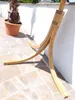 A wooden hammock stand is shown outdoors on a stone patio next to a potted palm tree. Produktbild-Vorschau