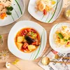A table setting with several plates of food, including soup, fruit salad, and a rolled dessert, along with cutlery and decorative flowers. Náhled obrázku produktu