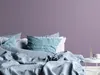 A bed with pillows and a duvet, with a purple wall in the background. Podgląd zdjęcia produktu