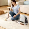 A woman is cleaning a carpet with a portable carpet cleaner. A dog is lying on the carpet in the background. Podgląd zdjęcia produktu