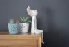 Two potted plants and a decorative figurine sit on a wooden surface against a gray wall. Anteprima dell’immagine prodotto