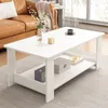 A white coffee table with a shelf is placed in a living room setting, next to a brown leather sofa. Náhled obrázku produktu