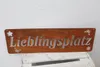 A rusty metal sign with the word "Lieblingsplatz" cut out, placed on a wooden crate. Produktbild-Vorschau