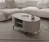 A modern living room scene featuring a white sectional sofa and a ribbed coffee table with storage shelves. Produktbild-Vorschau
