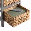 A close-up view of a woven basket drawer in a gray furniture unit, containing a green notebook and two pens. Produktbild-Vorschau