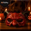 A red devil mask with black horns sits on a wooden surface, surrounded by pumpkins and lit candles, suggesting a Halloween theme. Produktbild-Vorschau