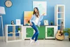 A young woman is dancing and listening to music in a room with blue walls and various furniture and decorations. Produktbild-Vorschau