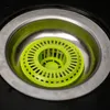 A close-up view of a green sink strainer placed in a stainless steel sink drain. Podgląd zdjęcia produktu