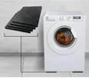 A washing machine and a stack of anti-vibration pads are shown against a concrete wall and tiled floor. Podgląd zdjęcia produktu