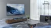 A living room scene with a TV, soundbar, and furniture, showcasing sound waves emanating from the soundbar. Anteprima dell’immagine prodotto