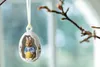 An Easter egg ornament with a bunny inside, hanging from a branch. Produktbild-Vorschau