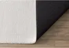 A close-up view of a rug on a wooden floor, showing the texture of the rug and its anti-slip backing. Produktbild-Vorschau