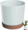 A light blue cylindrical planter with a brown saucer sits on a white background. A small green plant in a white pot is visible in the lower right corner. Náhľad obrázku produktu