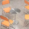 A round metal table with orange chairs around it, on a tiled floor. Produktbild-Vorschau