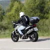 A person riding a motorcycle on a road with trees in the background. Podgląd zdjęcia produktu