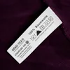 A close-up of a clothing care label attached to a purple fabric. Produktbild-Vorschau