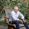 A man sits in a hanging chair outdoors, surrounded by greenery and red berries. Anteprima dell’immagine prodotto