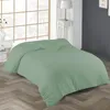 A light green duvet is laid out on a wooden floor in front of a large window with a white bedside table and lamp. Produktbild-Vorschau
