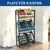 A black metal shelving unit holding various crates of drinks and produce, placed against a white wall. Produktbild-Vorschau