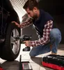 A man is using a cordless impact wrench to tighten the lug nuts on a car wheel. Produktbild-Vorschau