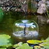A solar-powered fountain pump creating a water bubble in a pond with lily pads. Produktbild-Vorschau