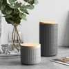 Two ceramic storage jars with wooden lids are displayed on a surface next to a vase of eucalyptus leaves. Produktbild-Vorschau