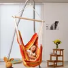 A young girl relaxing in a colorful hammock chair indoors, with a stuffed monkey and a stuffed rabbit nearby. Produktbild-Vorschau