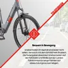 A close-up of an electric bicycle's front wheel and frame, with a road scene in the background and marketing text. Produktbild-Vorschau