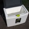 An open cooler box with a green latch, sitting on a paved surface with grass in the background. Produktbild-Vorschau