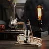 A wooden model of an electric guitar and a violin with its case are displayed on a table, along with an amplifier and a vintage-style light bulb. Voir les images du produit
