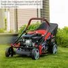 A red and black gas-powered lawnmower is shown on a green lawn in front of a house. Produktbild-Vorschau