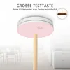 A smoke detector is shown mounted on a ceiling, with a broomstick extending from it, suggesting ease of testing. The background shows a blurred interior of a home with furniture. Produktbild-Vorschau