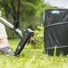 A person using a weed remover tool in a grassy outdoor area next to a large black bin. Produktbild-Vorschau