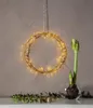 A gold LED light wreath hangs on a wall, with a potted amaryllis bulb in a glass bowl on a table below. Podgląd zdjęcia produktu