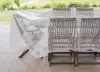 A transparent protective cover is draped over a wooden outdoor table and chairs, set on a tiled patio with a blurred green field in the background. Anteprima dell’immagine prodotto