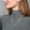 A woman wearing a grey turtleneck sweater and two silver necklaces. Podgląd zdjęcia produktu