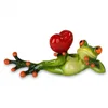 A ceramic figurine of a frog holding a red heart, lying on its back. Produktbild-Vorschau