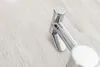 A chrome bidet sprayer is placed on a light wood-grain surface. Podgląd zdjęcia produktu