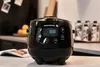 A black rice cooker is shown on a kitchen counter with an open book in front of it. There are also some bottles in the background. Anteprima dell’immagine prodotto