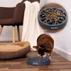 A small dog eating from a slow feeder bowl on a wooden floor, with a dog bed and a chair in the background. Náhľad obrázku produktu