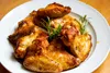 A close-up shot of a plate of cooked chicken wings, garnished with rosemary and parsley, on a wooden table. Produktbild-Vorschau