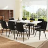 A dining set with a marble-top table and black velvet chairs in a well-lit room with a large window overlooking a garden.