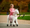 A young girl rides a white toy horse with pink accents in a park setting. Anteprima dell’immagine prodotto