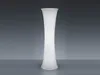 A tall, white, hourglass-shaped floor lamp stands against a plain gray background. Produktbild-Vorschau