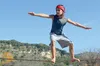 A young person is slacklining outdoors with a wooded hill and blue sky in the background. Produktbild-Vorschau