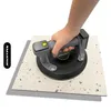A hand holding a vacuum lifter on a tile. Produktbild-Vorschau