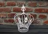 A white decorative crown is placed on a dark wooden surface in front of a brick wall. Produktbild-Vorschau